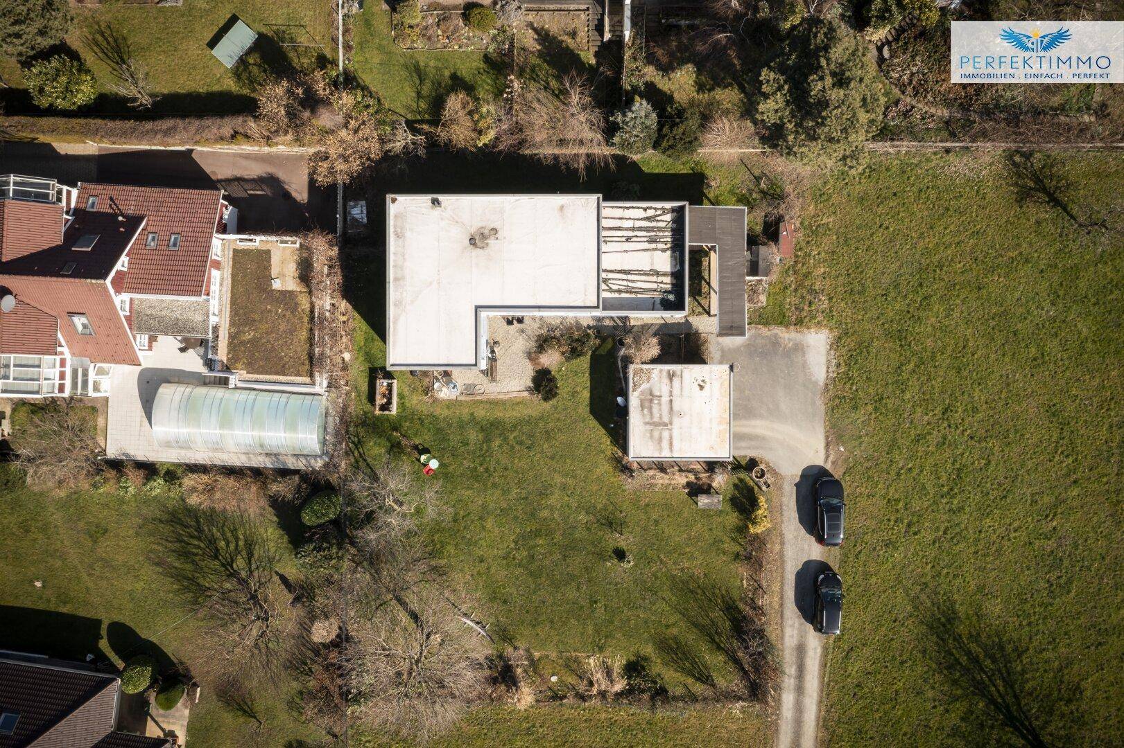 Vogelperspektive des Grundstücks mit Haus, Carport und umliegender Bebauung.