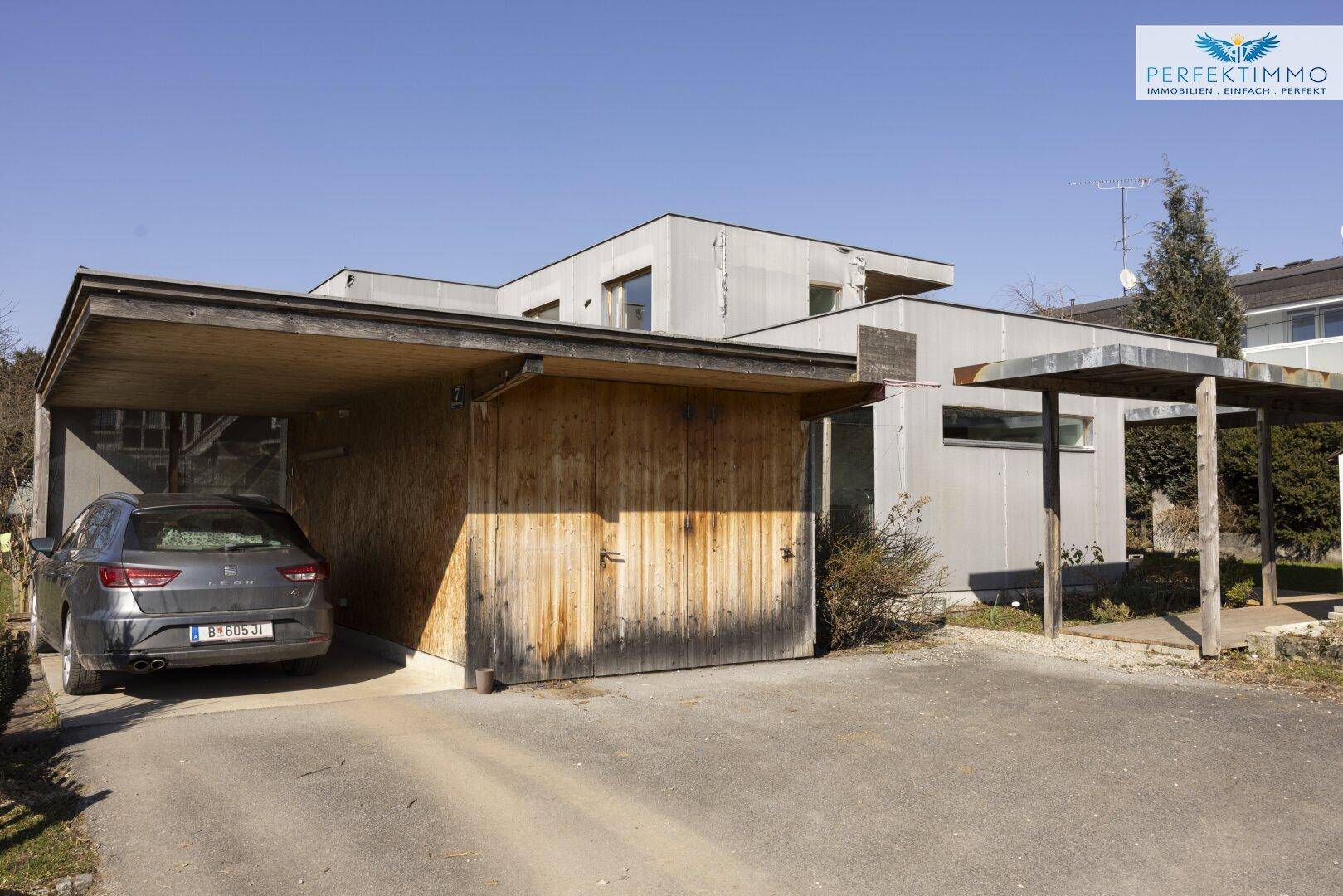 Carport und Garage des Hauses mit Holztoren und Stellplatz.
