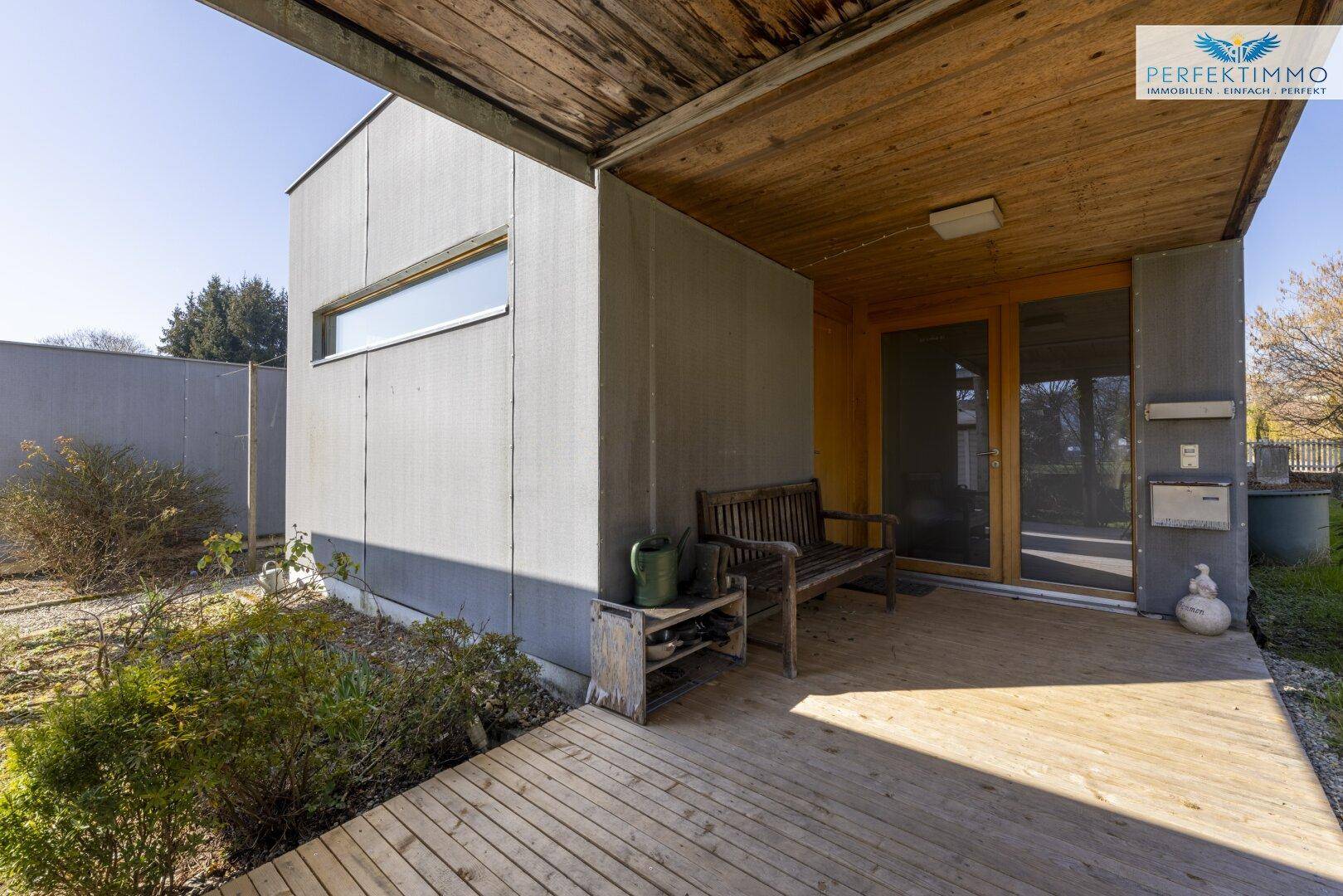 Eingangsbereich des modernen Hauses mit Holzbank und überdachtem Zugang.