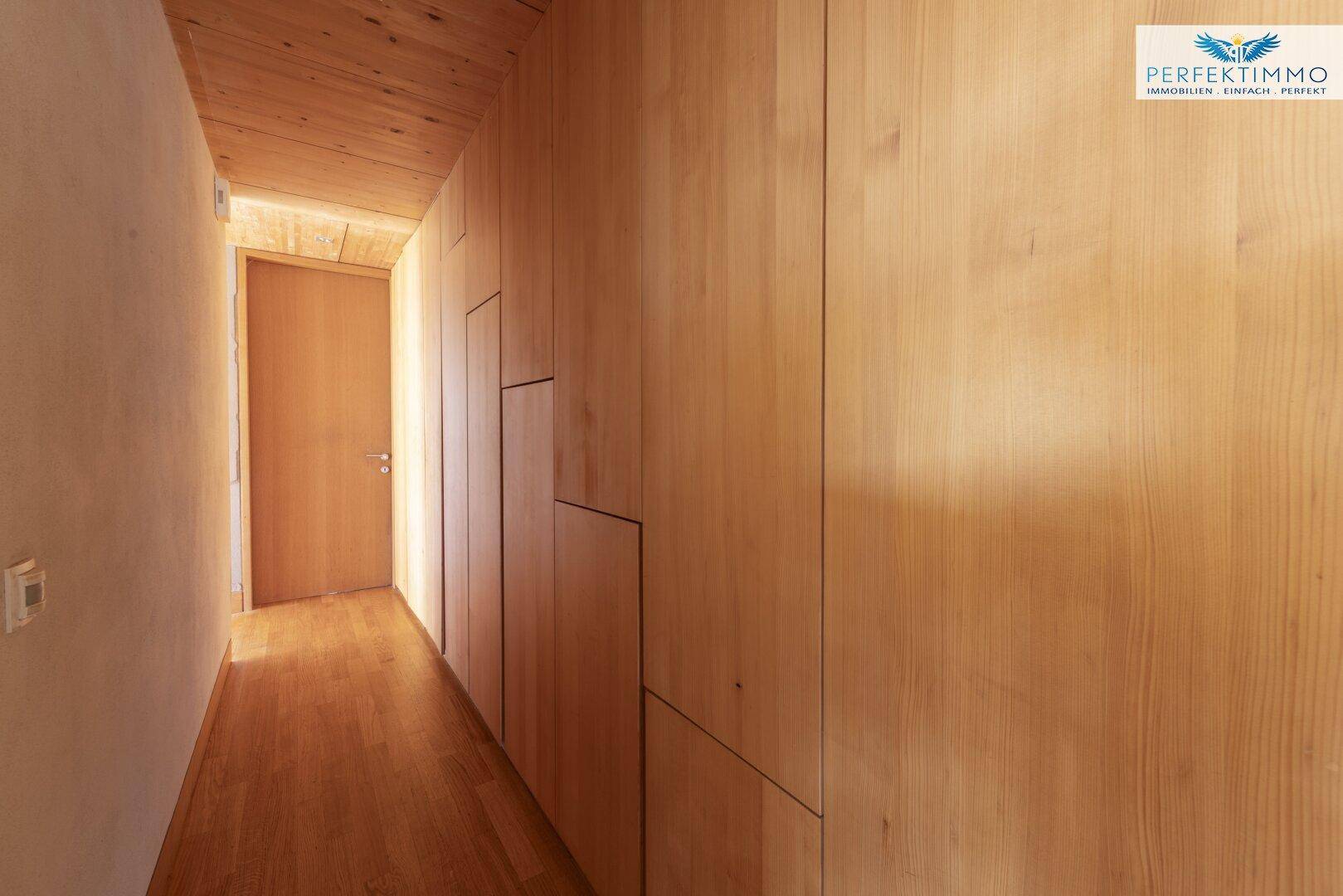 Schmaler Flur mit Holzverkleidung an den Wänden und Holzboden.
