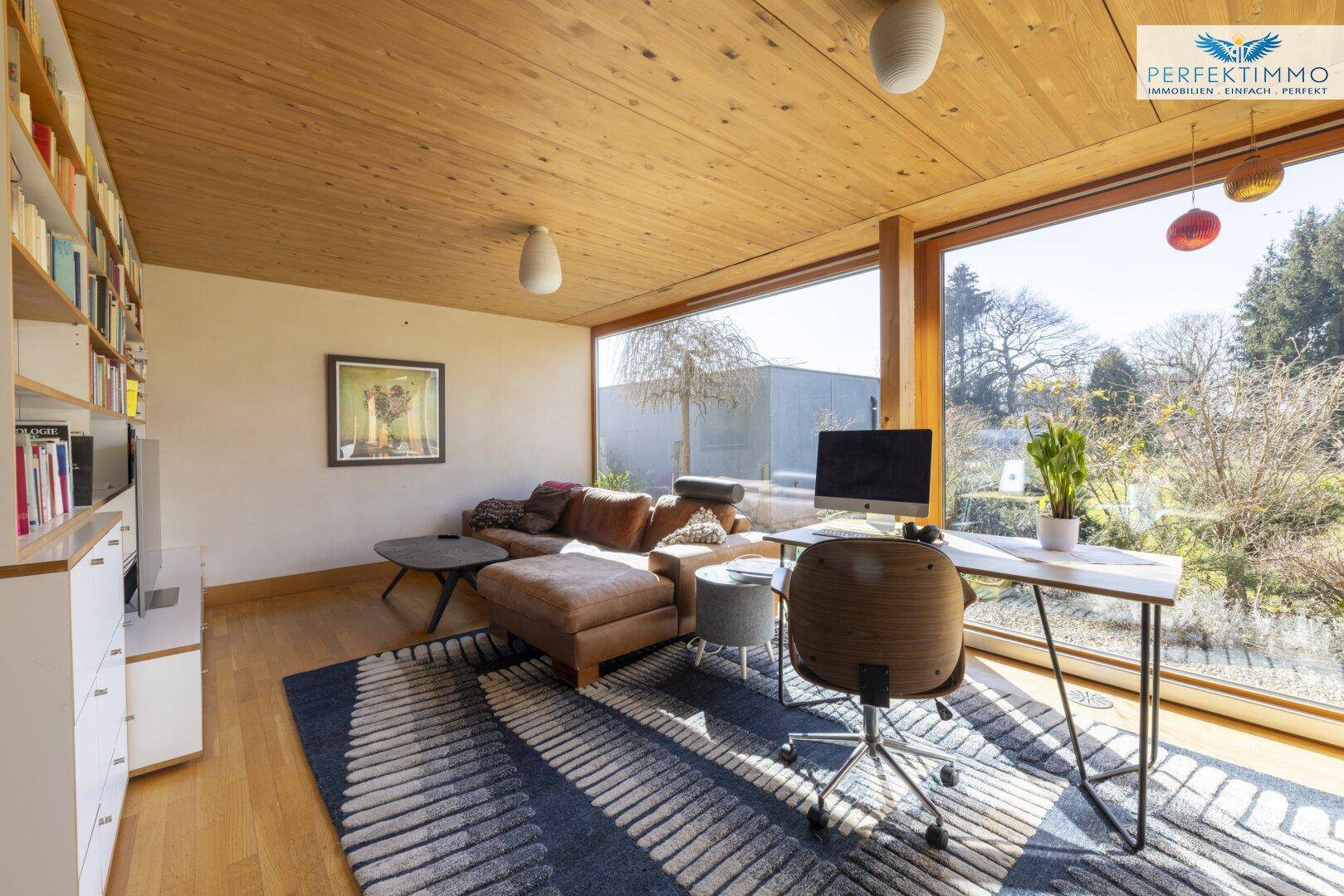 Helles Wohnzimmer mit großen Fenstern, Holzbalkendecke und Blick ins Grüne.
