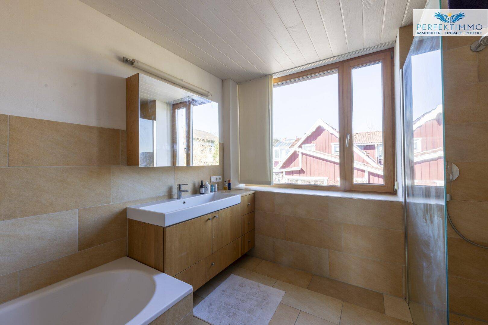 Geräumiges Badezimmer mit Badewanne, Dusche, Waschtisch und Fenster.
