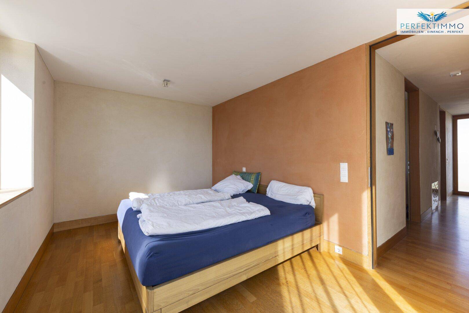 Helles Schlafzimmer mit Holzboden, Akzentwand und Zugang zum Flur.