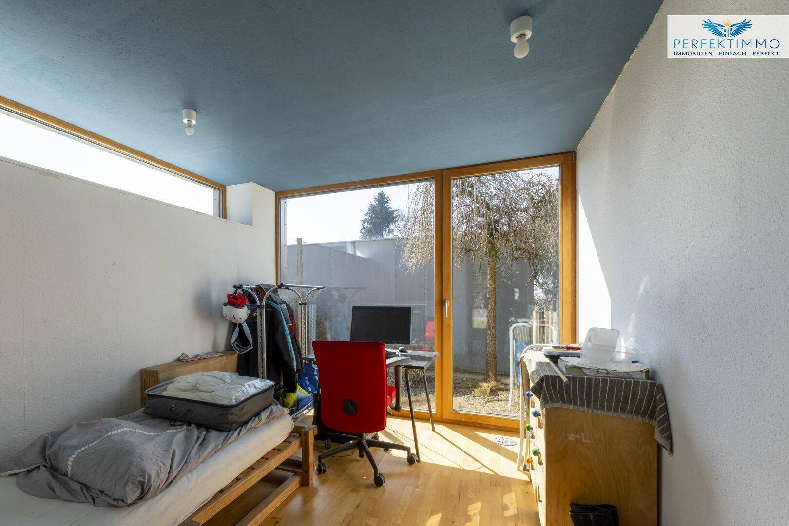 Helles Zimmer mit Einzelbett, Schreibtisch und großen Fenstern zum Garten.