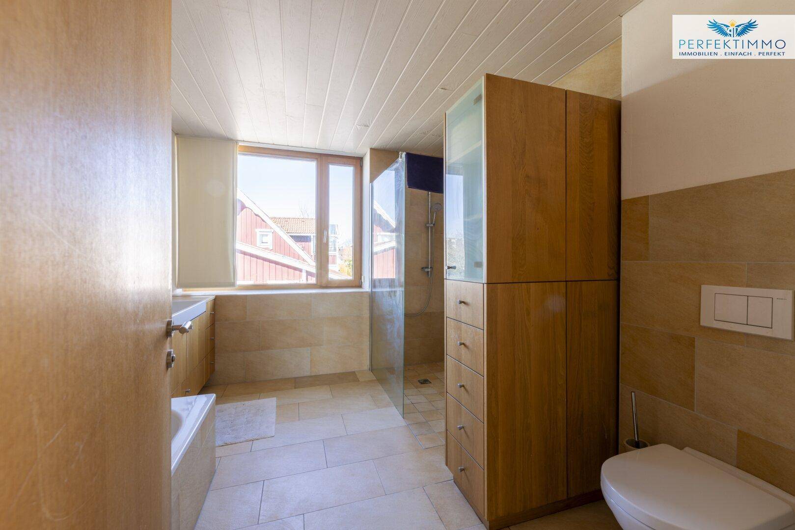 Helles Badezimmer mit Dusche, WC, Waschtisch und Holzschränken.