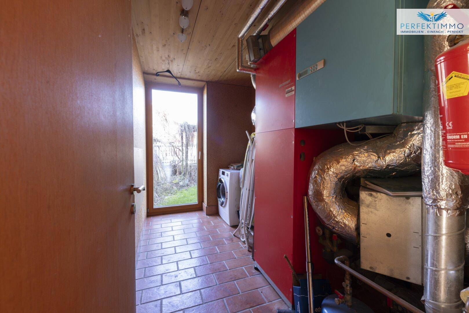 Hauswirtschaftsraum mit Heizungsanlage, Waschmaschine und Zugang nach draußen.