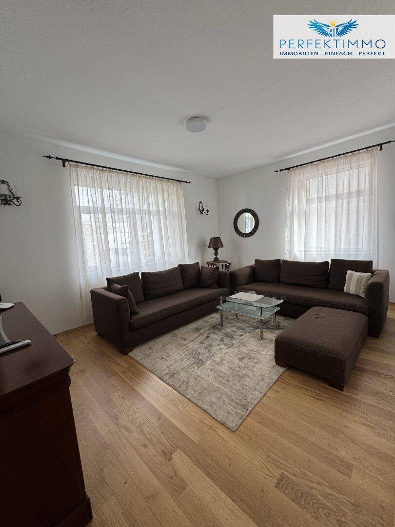 Gemütliches Wohnzimmer mit zwei braunen Sofas, Holzboden und einem hellen Teppich.