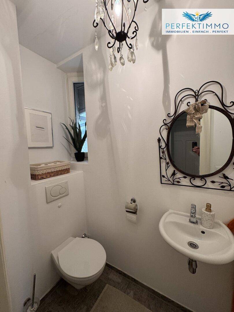 Kleines Gäste-WC mit wandhängender Toilette, kleinem Waschbecken und Fenster.