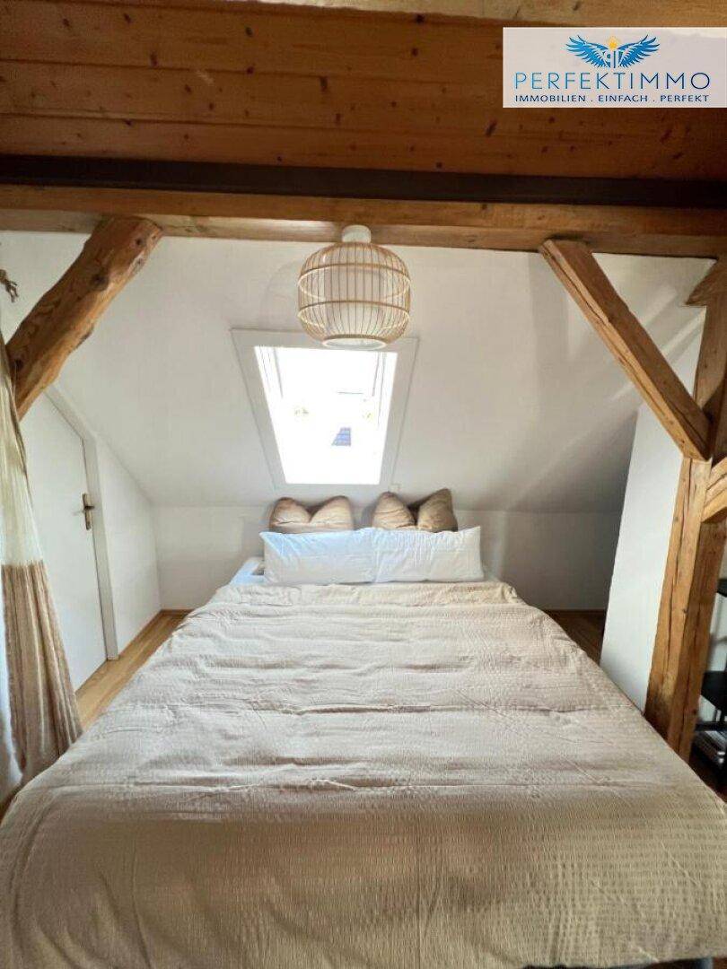 Gemütliches Schlafzimmer im Dachgeschoss mit sichtbaren Holzbalken und Dachfenster.