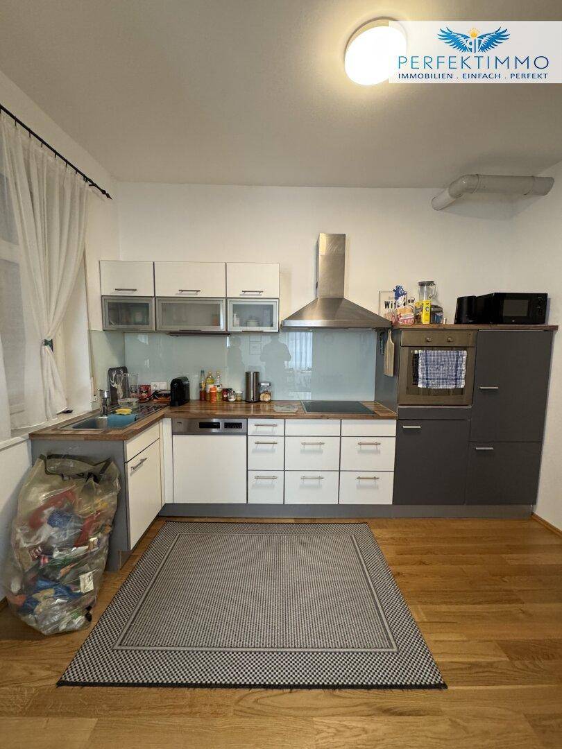 Moderne Küche mit weißen und grauen Schränken, Holzboden und integrierten Geräten.