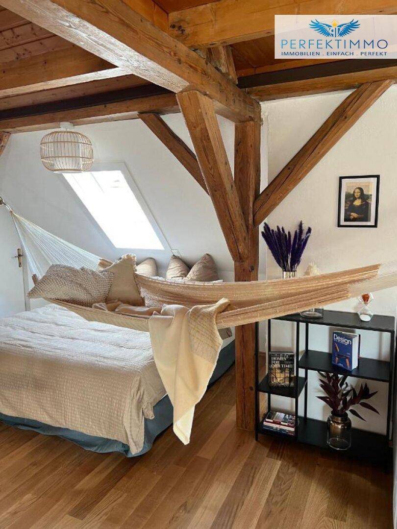 Dachgeschoss-Schlafzimmer mit Holzbalken, Hängematte und Dachfenster für viel Licht.