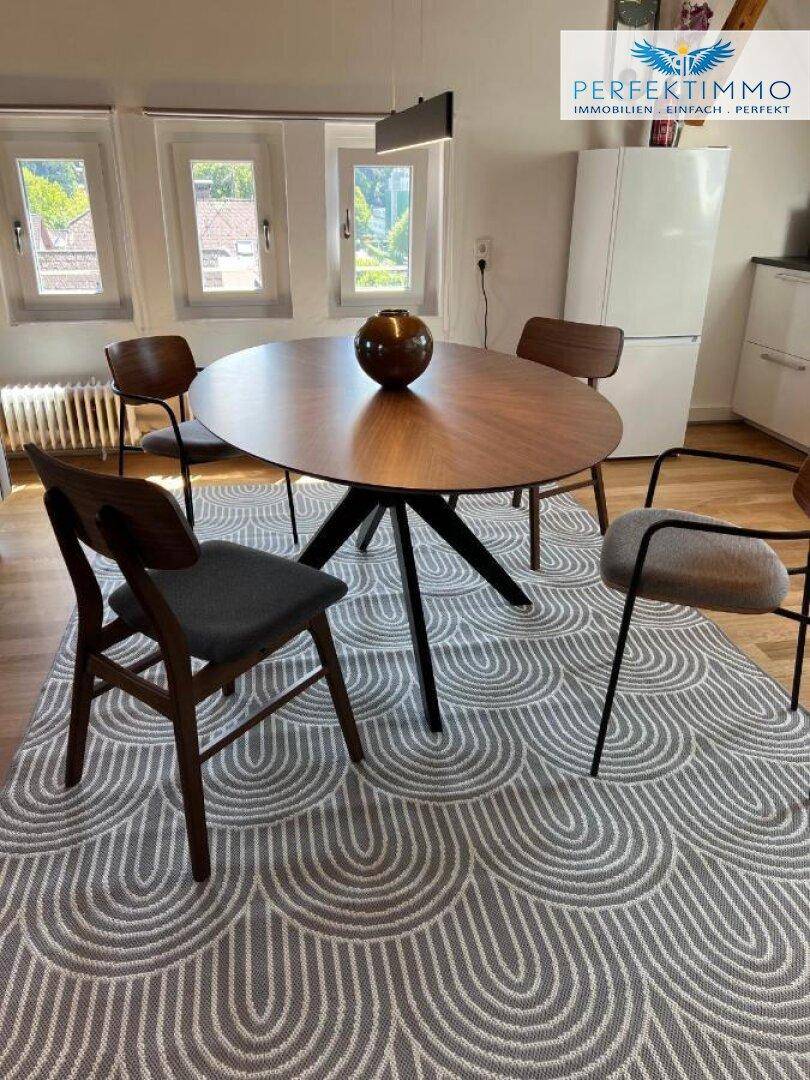 Moderner Essbereich mit ovalem Holztisch, Designerstühlen und einem Kühlschrank im Hintergrund.
