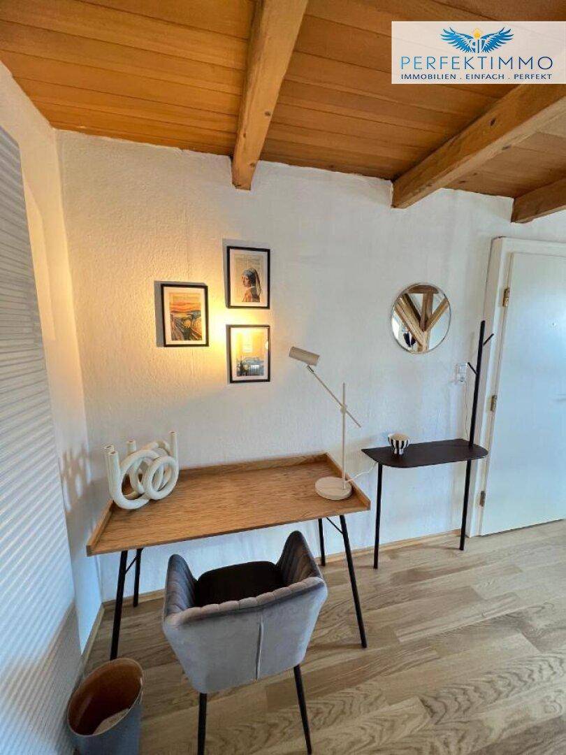 Arbeitsbereich im Dachgeschoss mit Holzschreibtisch, modernem Stuhl und Holzdecke.