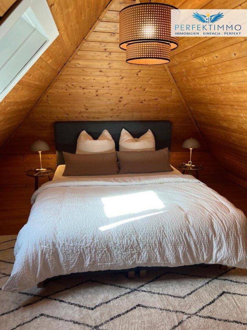 Schlafzimmer im Dachgeschoss mit Holztäfelung, Doppelbett und Dachfenster.