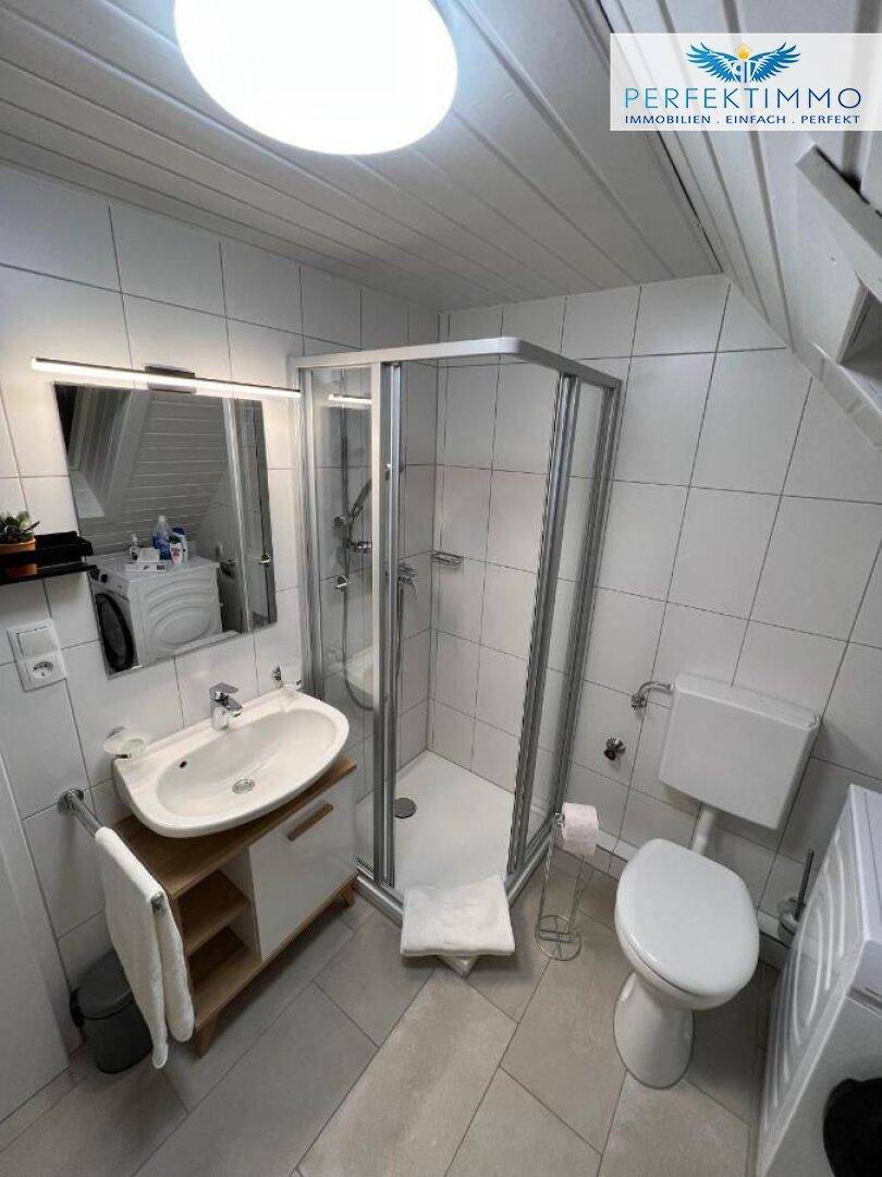 Helles Badezimmer im Dachgeschoss mit Duschkabine, Waschbecken und schräger Decke.