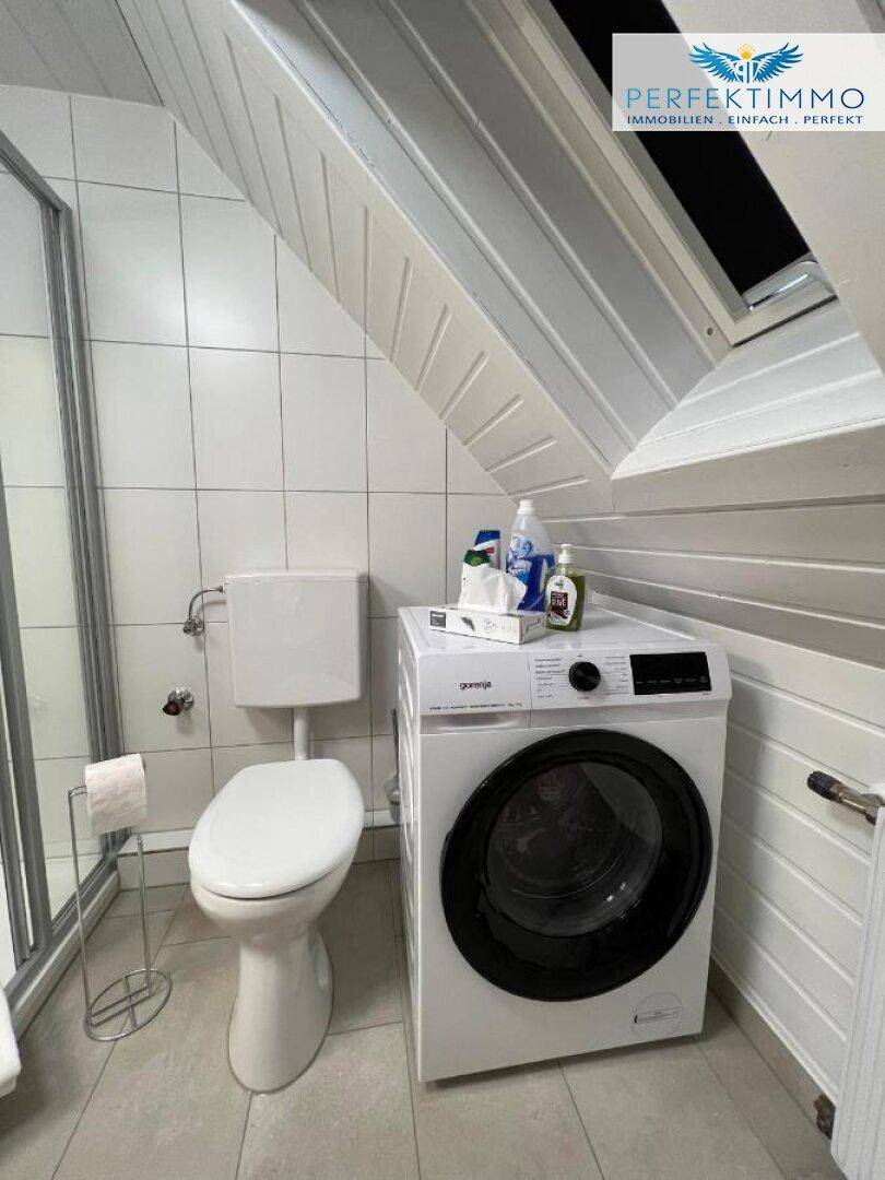 Badezimmer im Dachgeschoss mit Toilette und Waschmaschine unter der Dachschräge.