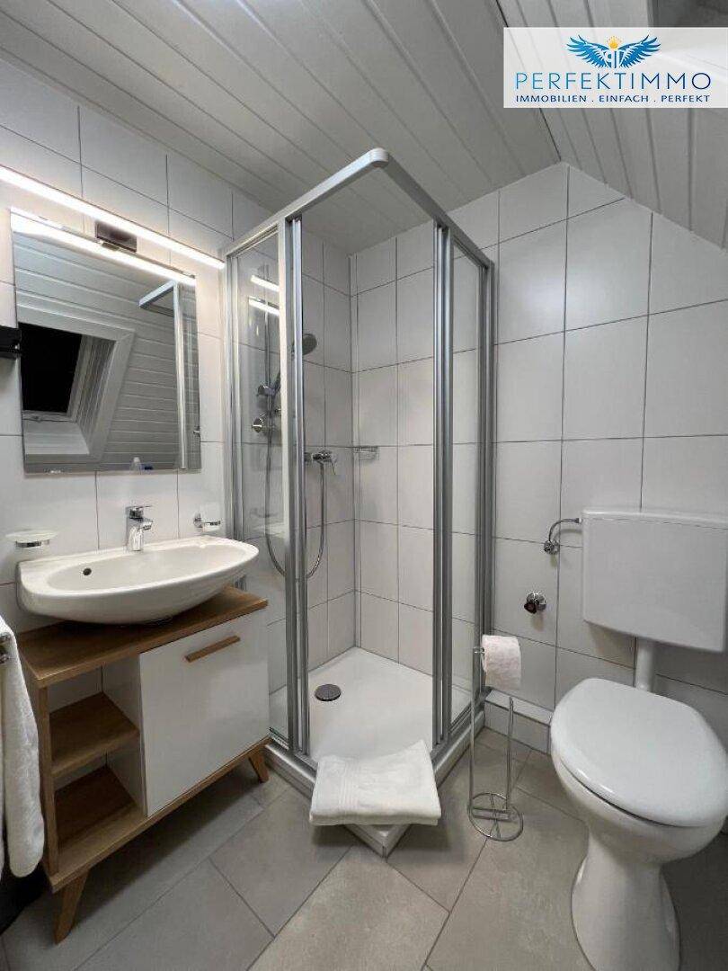 Modernes Badezimmer im Dachgeschoss mit Duschkabine, Waschbecken und Spiegelschrank.