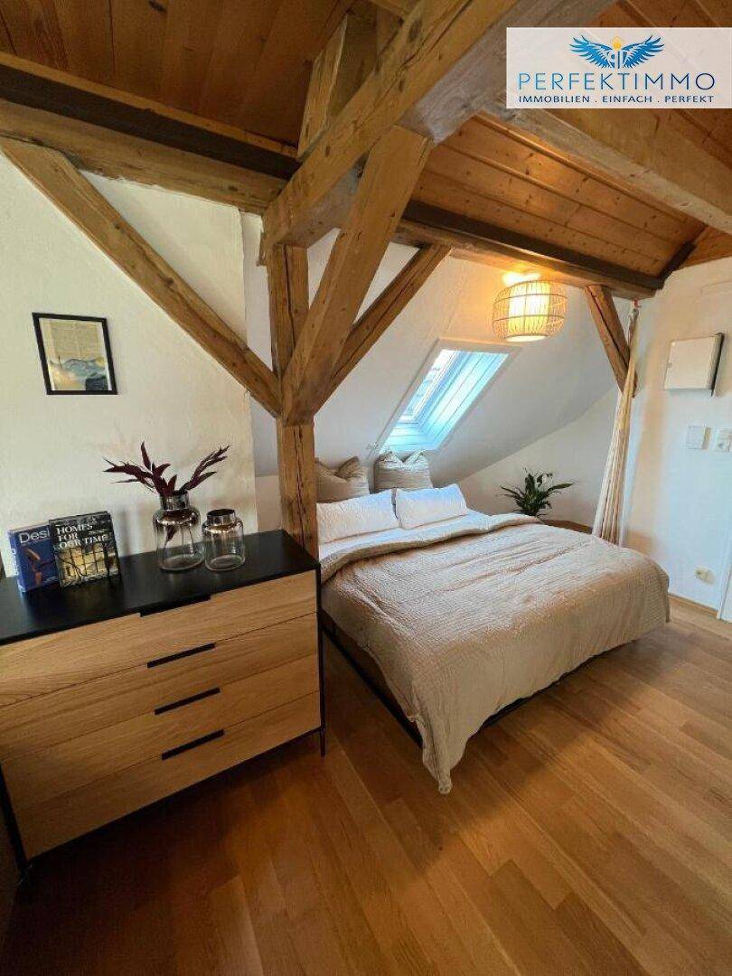 Schlafzimmer im Dachgeschoss mit Holzbalken, Bett und moderner Kommode.