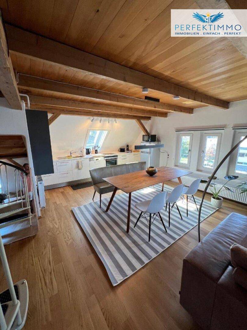 Großzügiger offener Wohn-Essbereich mit Küche, Holzboden und sichtbaren Dachbalken.
