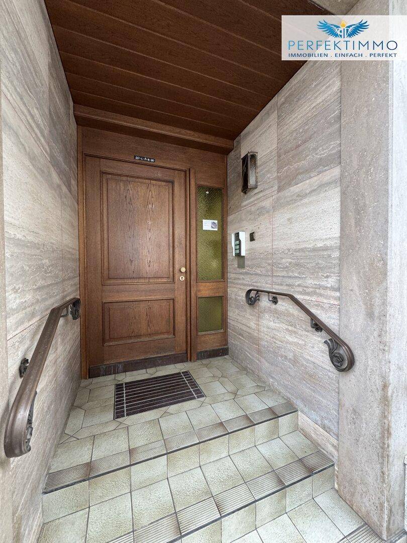 Eingangsbereich mit Holztür, Steinverkleidung an den Wänden und Handläufen für den Zugang.