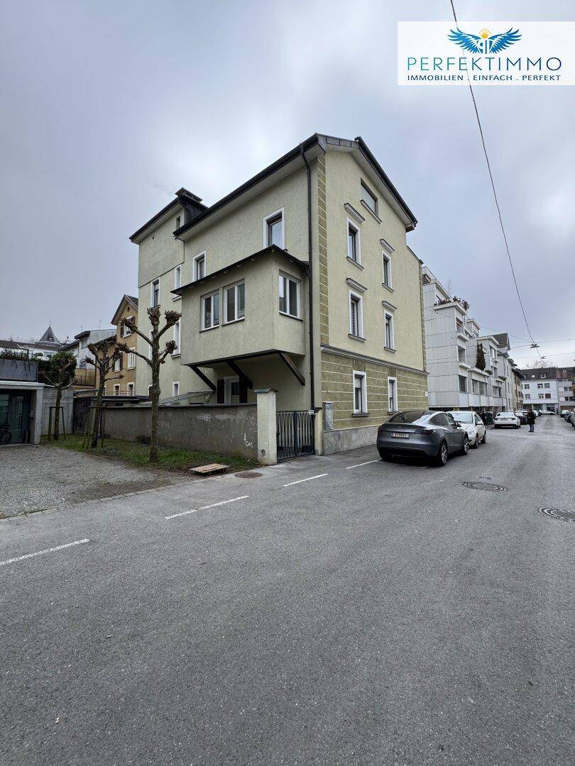 Seitenansicht des Gebäudes mit heller Fassade und Fenstern, umgeben von einer ruhigen Straße.
