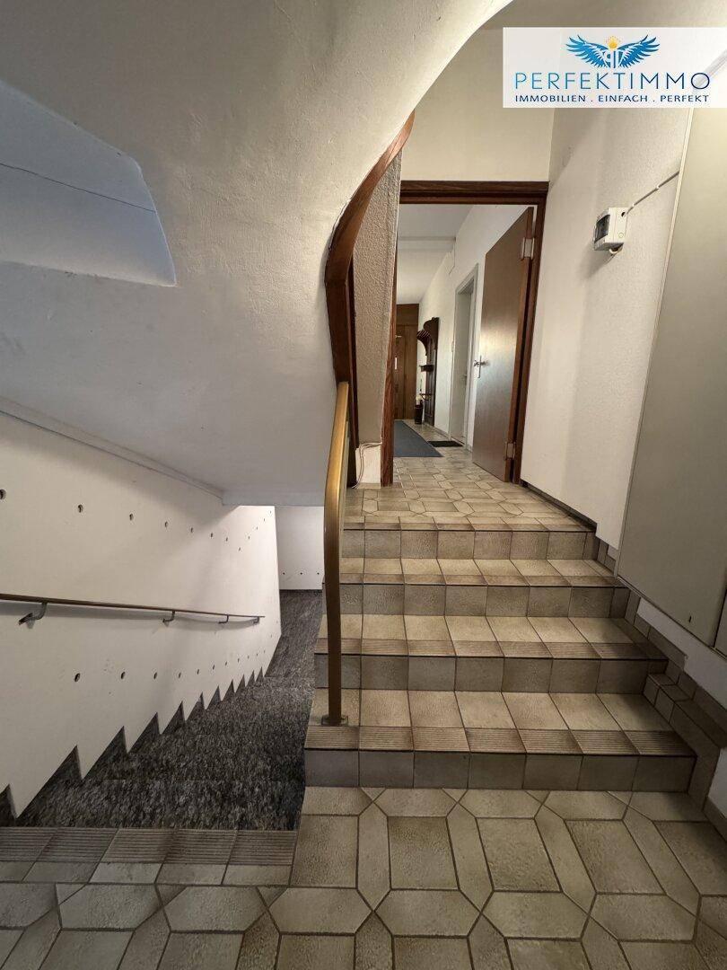 Treppenhaus mit gefliesten Stufen und einem Geländer, das zu den oberen Etagen führt.
