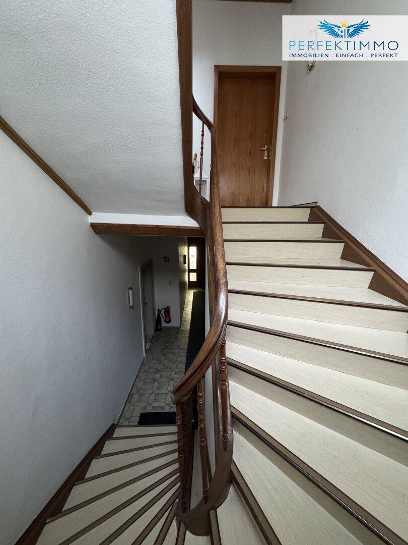 Wendeltreppe mit Holzgeländer und hellen Stufen, die zu den oberen Stockwerken führt.