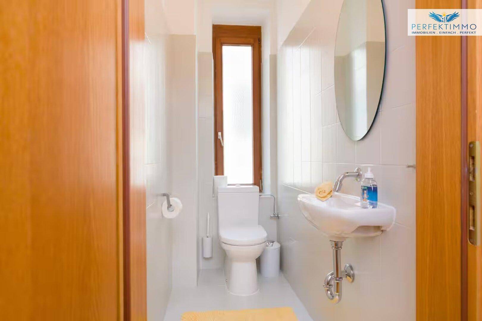 Separates WC mit Fenster, wandmontierter Toilette und kleinem Handwaschbecken.
