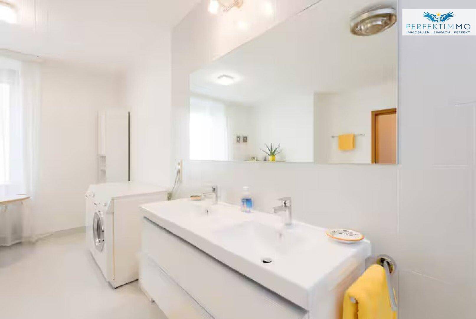 Modernes Badezimmer mit Doppelwaschbecken, großer Spiegelfläche und Waschmaschine.