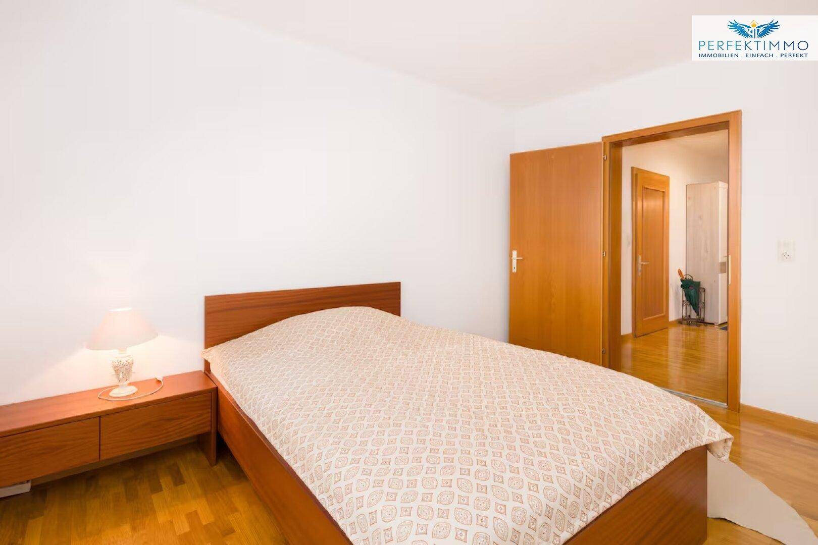 Schlafzimmer mit Holzboden, Einzelbett und Nachttisch, mit Blick in den Flur.