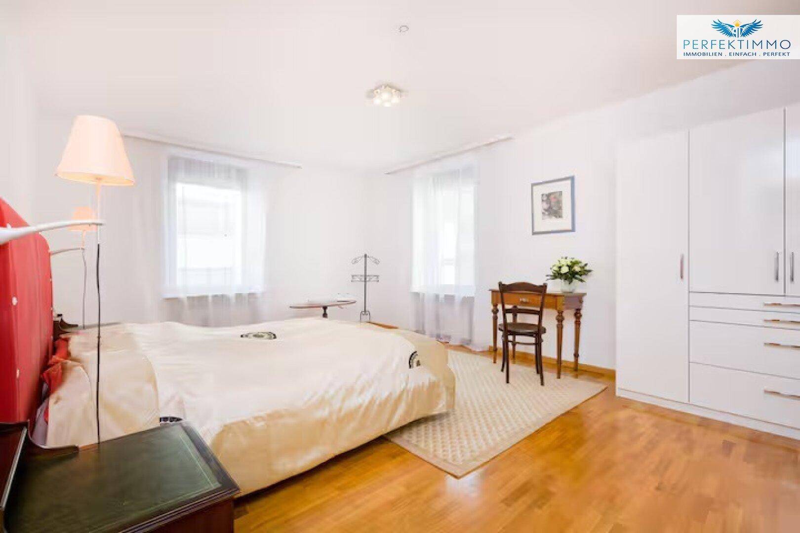 Helles Schlafzimmer mit Holzboden, großem Bett, Kleiderschrank und zwei Fenstern.