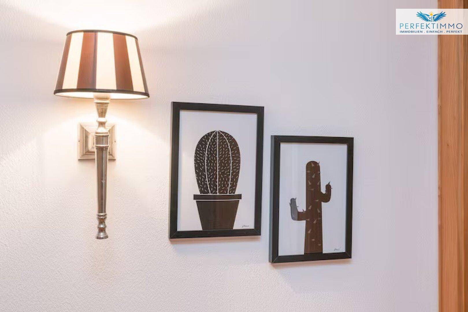 Wanddekoration mit Kaktusbildern und einer eleganten Wandleuchte in einem Innenraum.