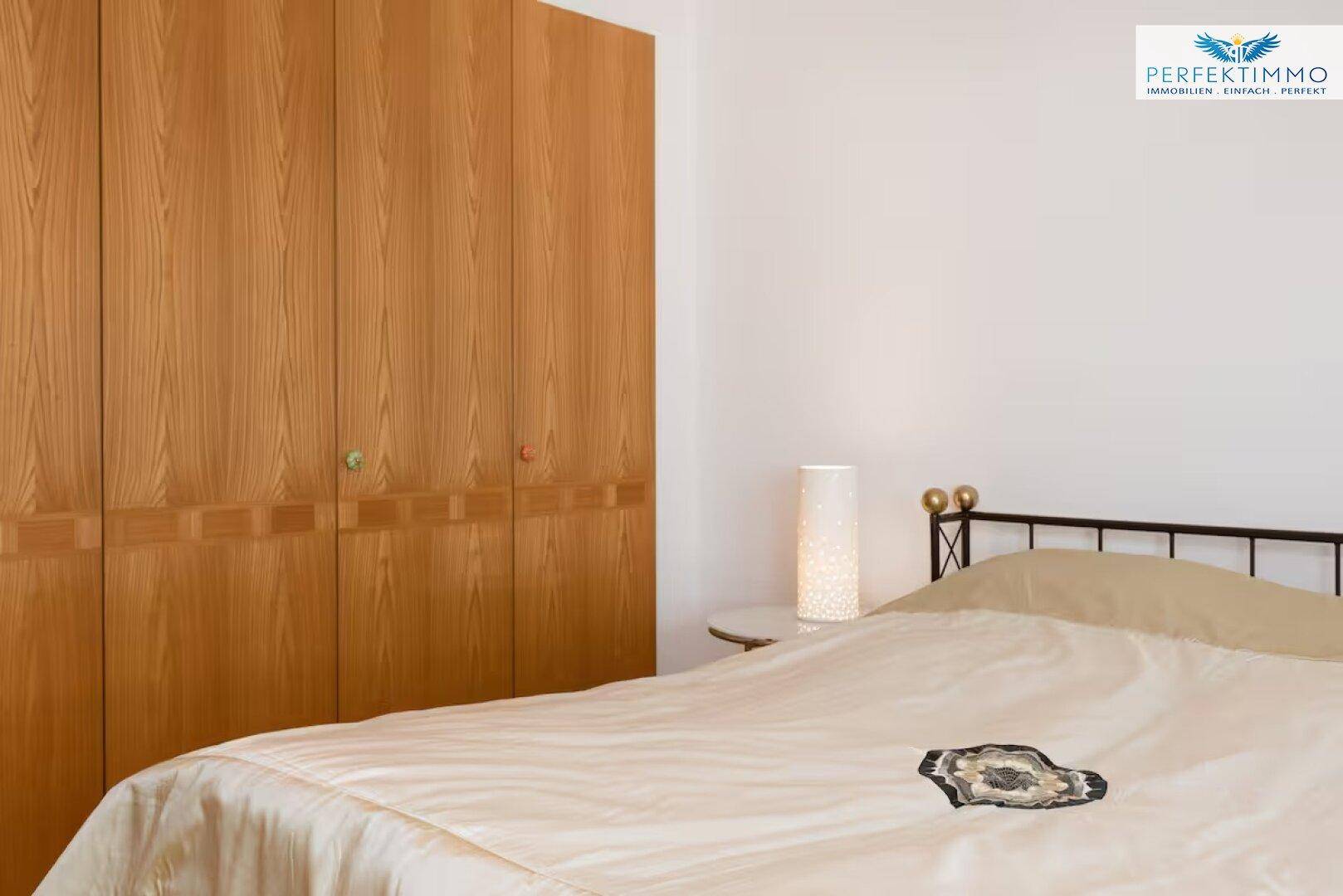 Schlafzimmer mit großem Holzkleiderschrank und einem gemütlichen Bett mit Nachttischlampe.