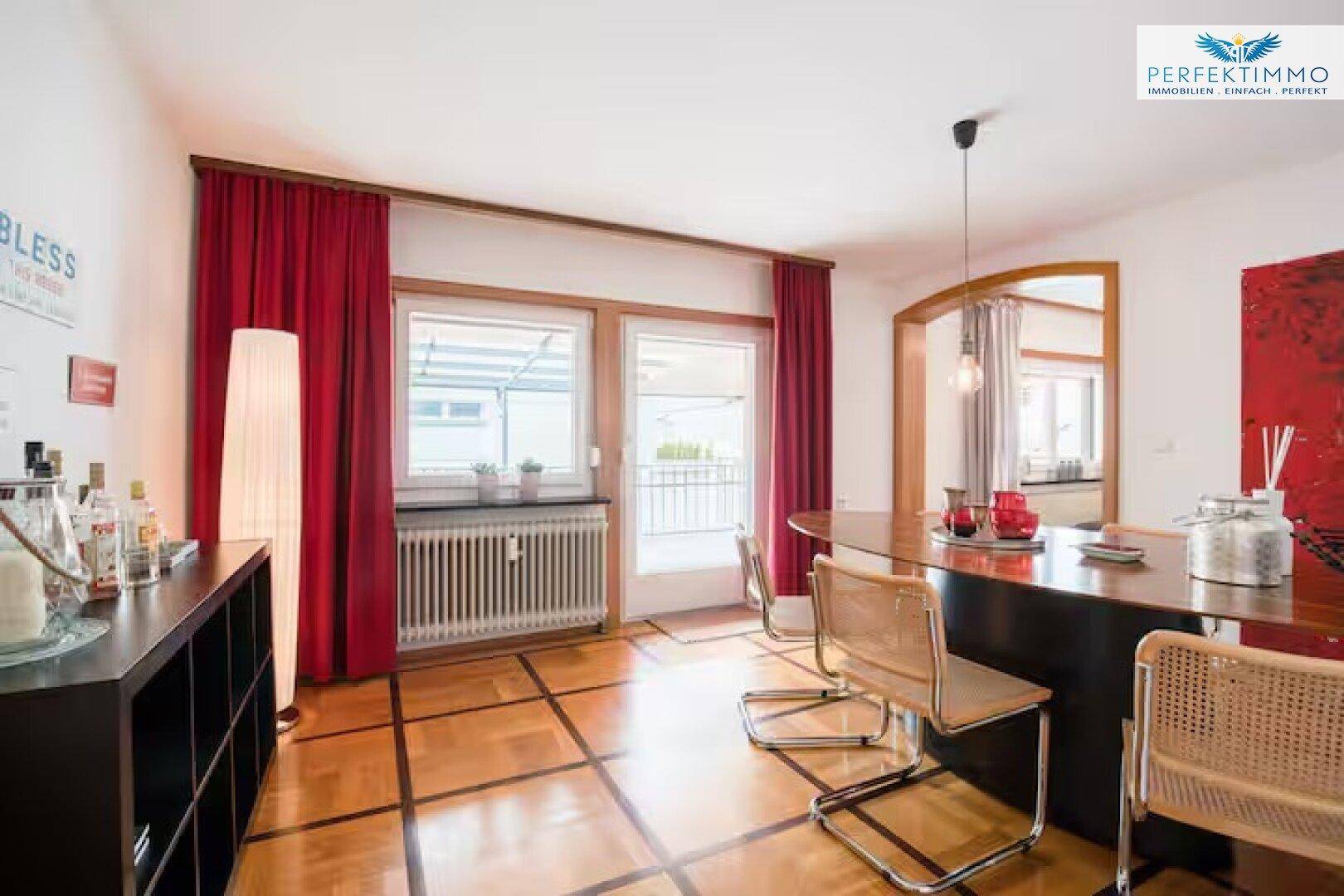 Essbereich mit Zugang zu einem kleinen Balkon, Parkettboden und roten Vorhängen.