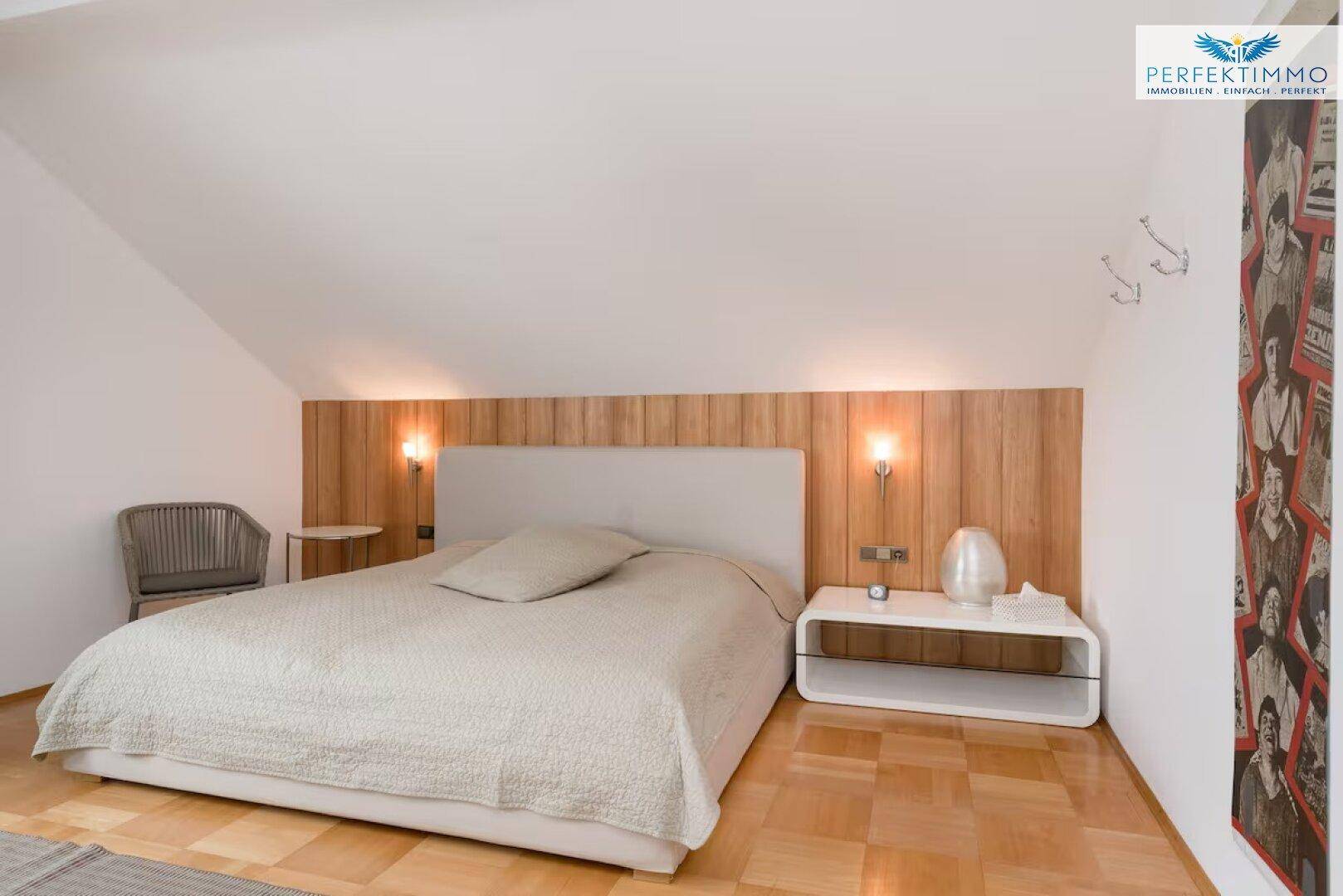 Gemütliches Schlafzimmer mit Holzwandverkleidung hinter dem Bett und Dachschräge.