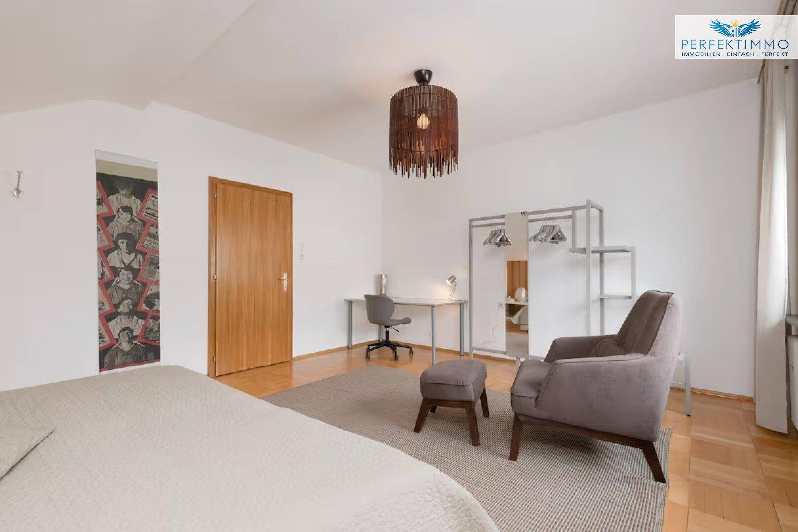 Schlafzimmer mit Dachschräge, Schreibtisch, Sessel und offenem Kleiderständer.