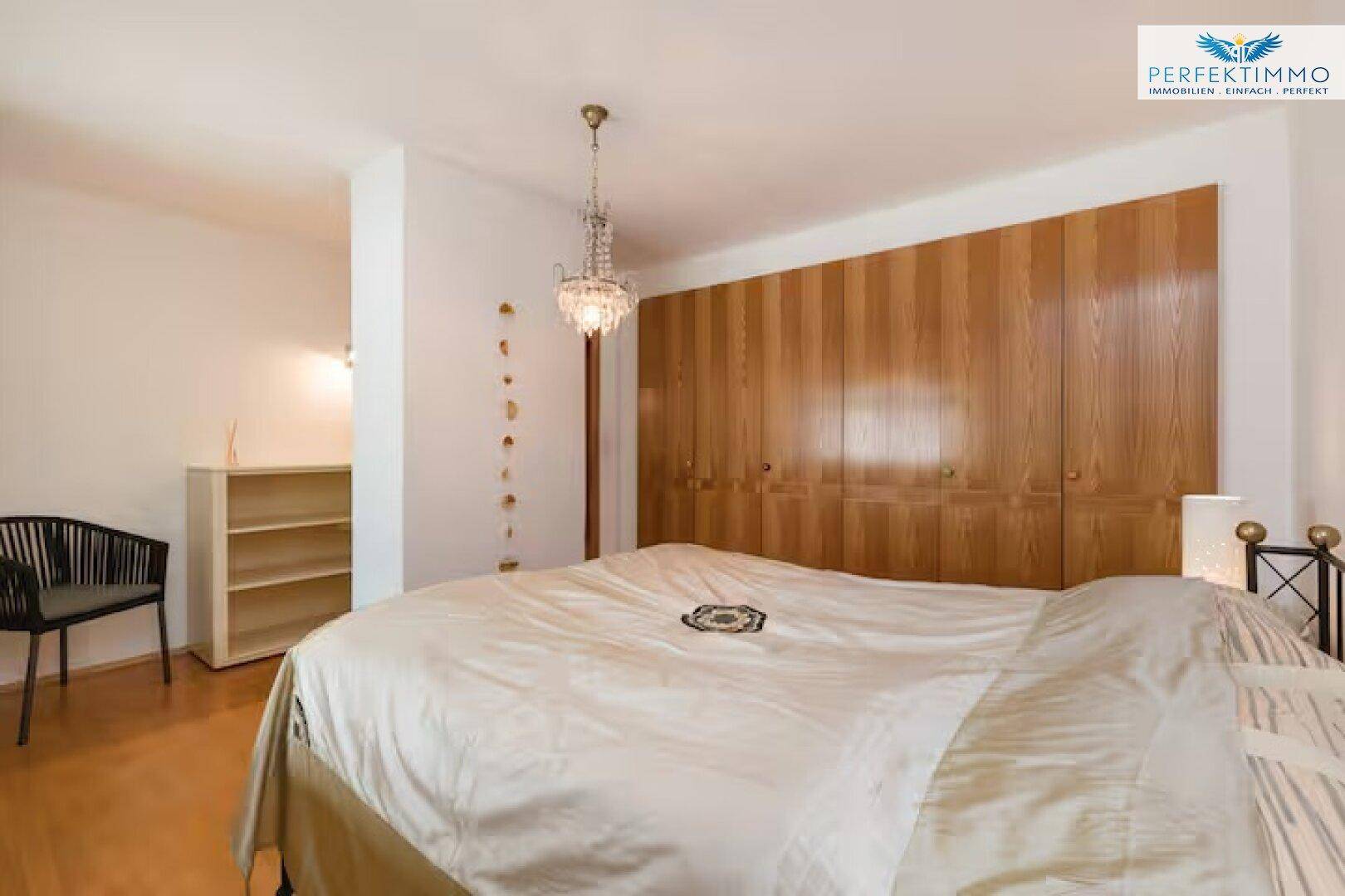 Schlafzimmer mit großem Holzkleiderschrank, Doppelbett und Kronleuchter.