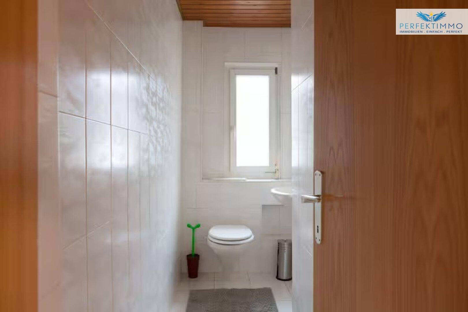 Kleines WC mit Fenster, Wandfliesen und Holzdecke.