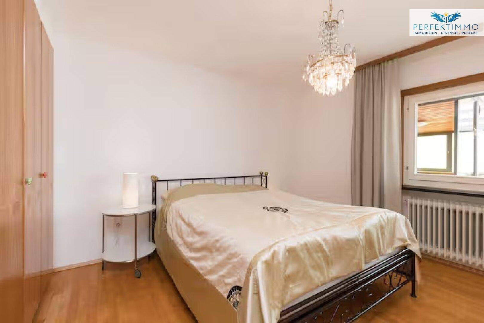 Schlafzimmer mit Doppelbett, Nachttisch und Fenster mit Heizkörper.