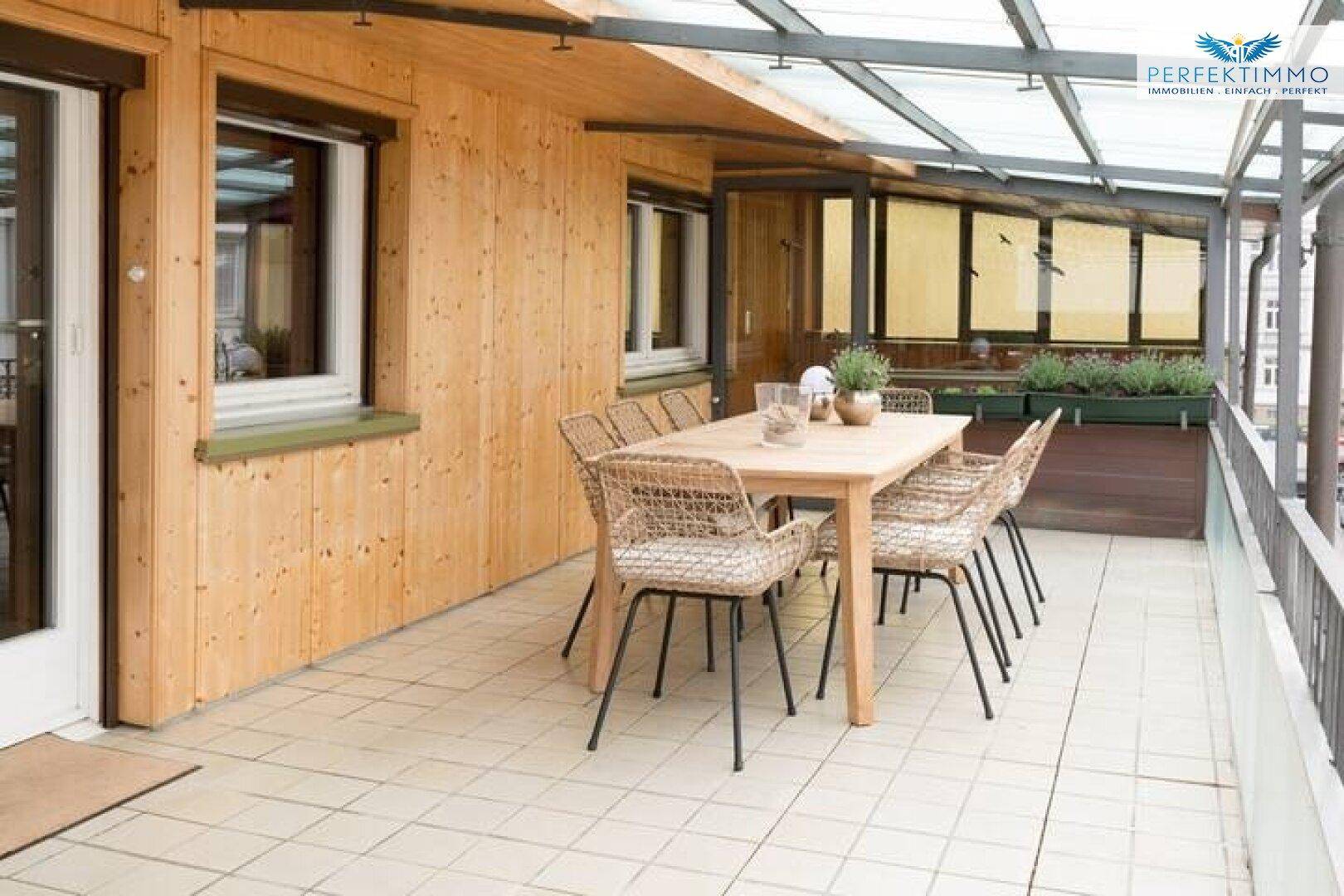 Große Terrasse mit Holzwandverkleidung, Esstisch und Stühlen unter einer Überdachung.