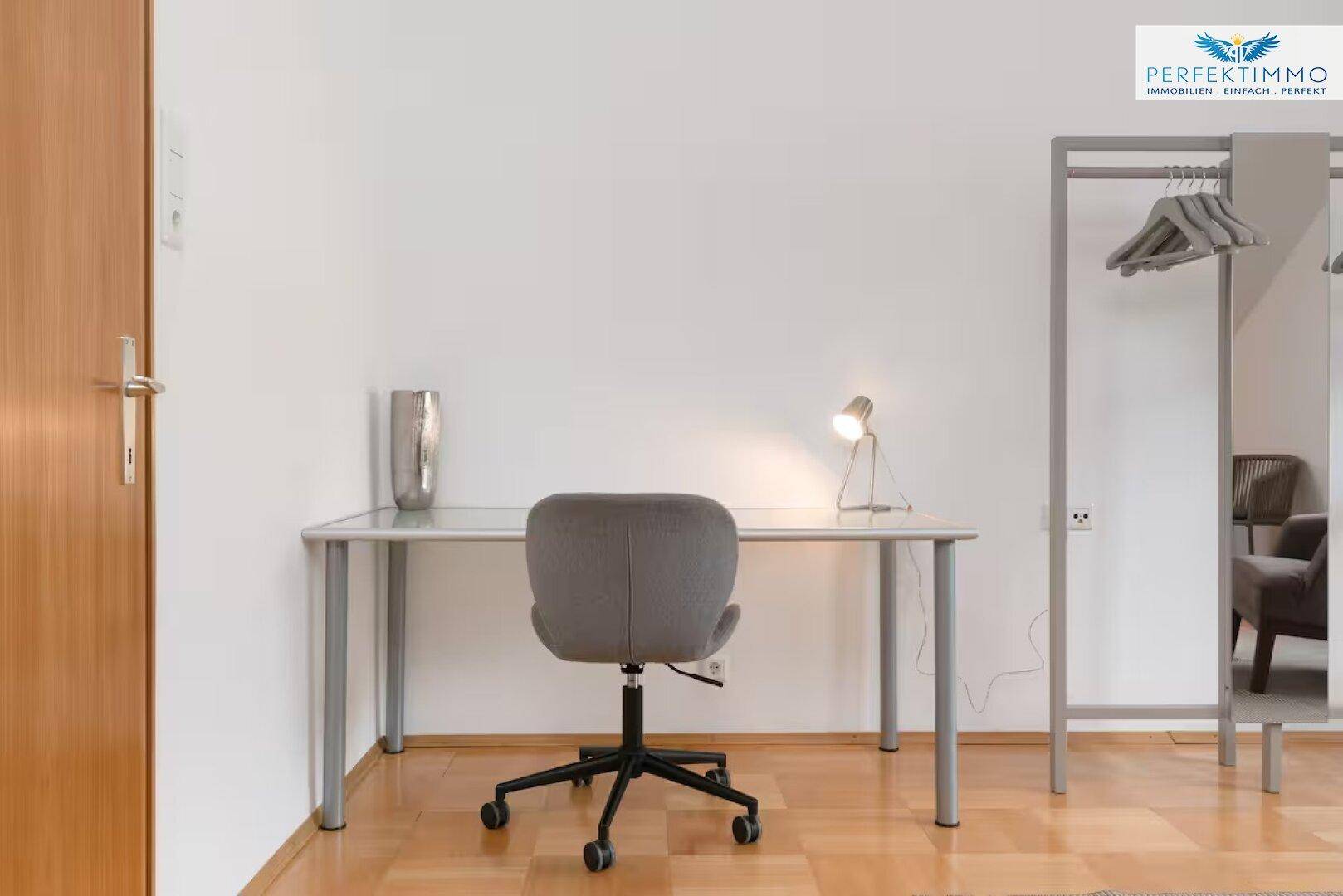 Schreibtisch mit Bürostuhl und Lampe in einem hellen Raum.