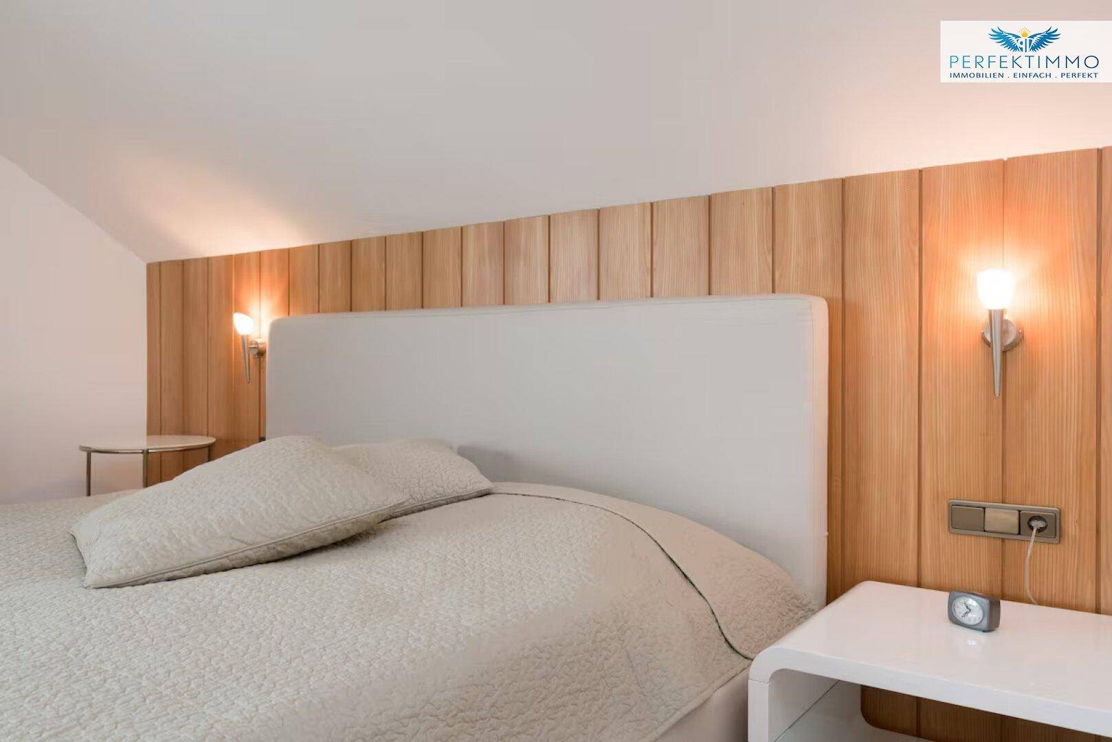 Gemütliches Schlafzimmer mit Holzwandverkleidung hinter dem Bett und Wandleuchten.