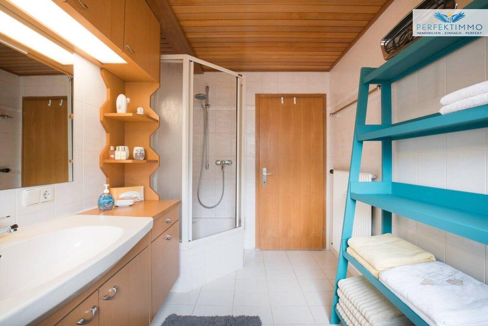 Badezimmer mit Duschkabine, Waschbecken, Holzdecke und Handtuchregal.