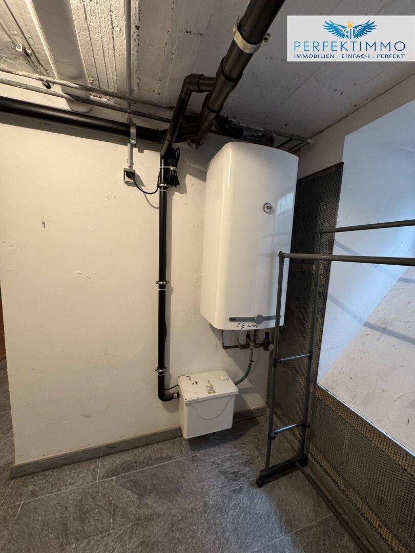 Funktionaler Hauswirtschaftsraum im Keller mit Warmwasserbereiter und sichtbaren Leitungen.