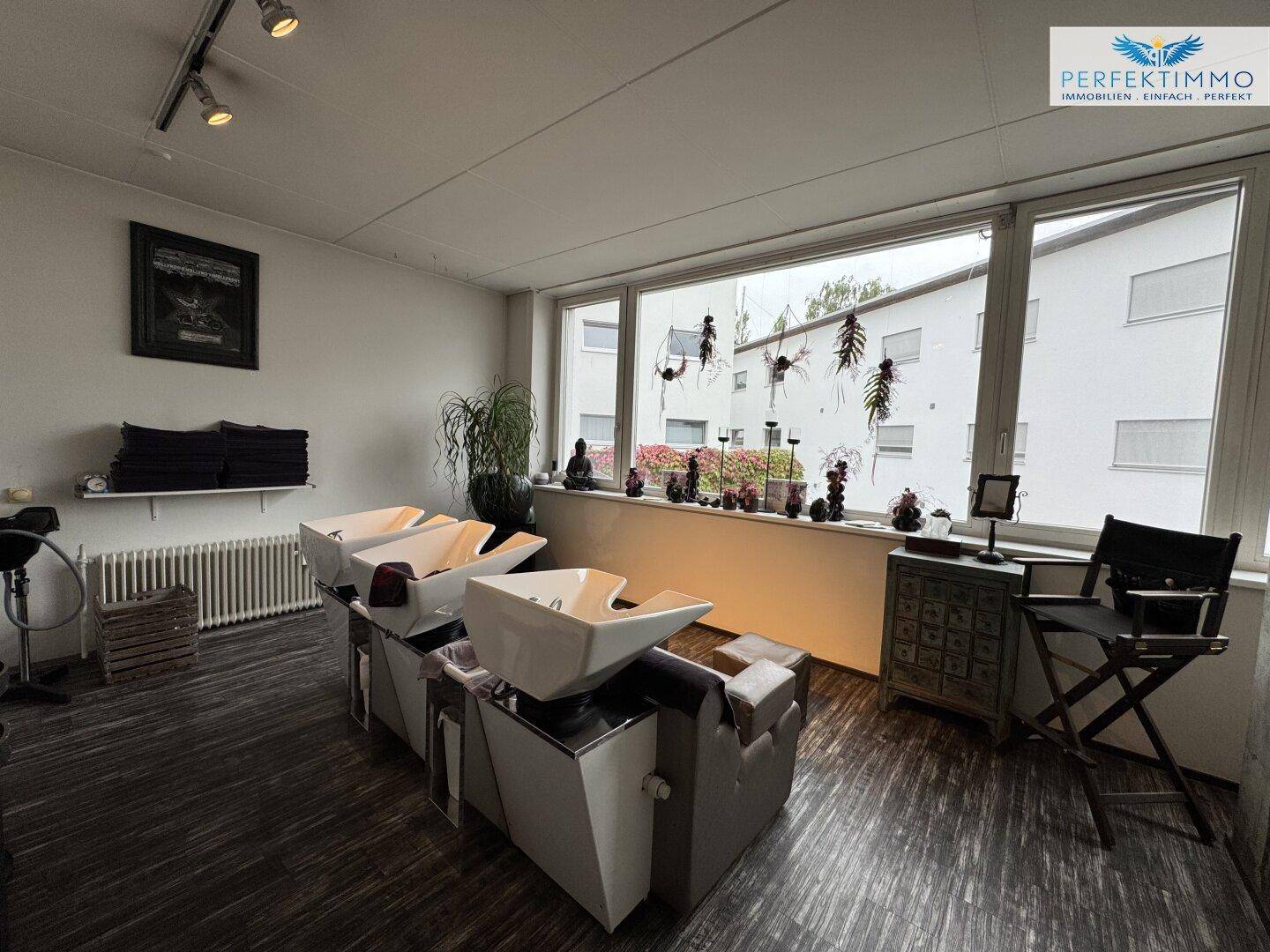 Friseursalon mit Haarwaschbecken, großen Fenstern und einem Heizkörper.
