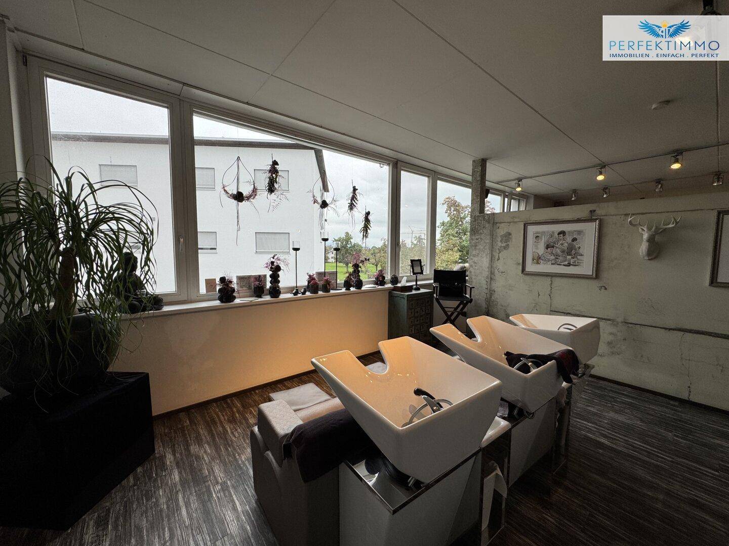 Weitere Ansicht des Friseursalons mit Haarwaschbecken und großen Fenstern.