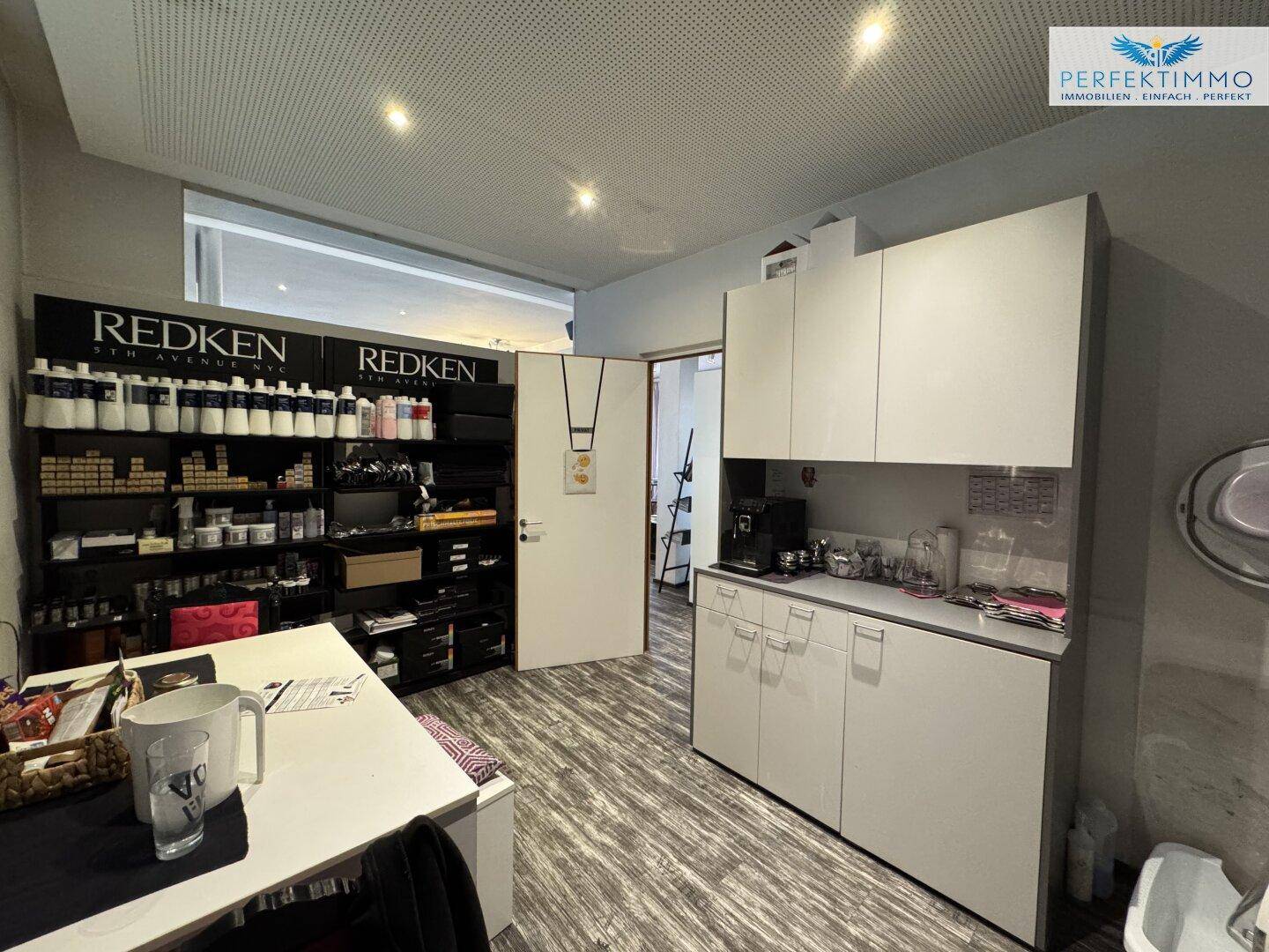 Kleine Küche oder Personalraum mit Schränken, Kaffeemaschine und Produktregalen.