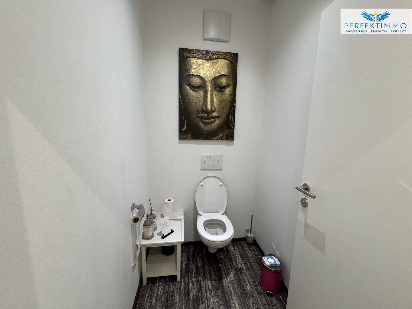 Toilettenraum mit wandhängendem WC und einem Buddha-Kunstwerk.