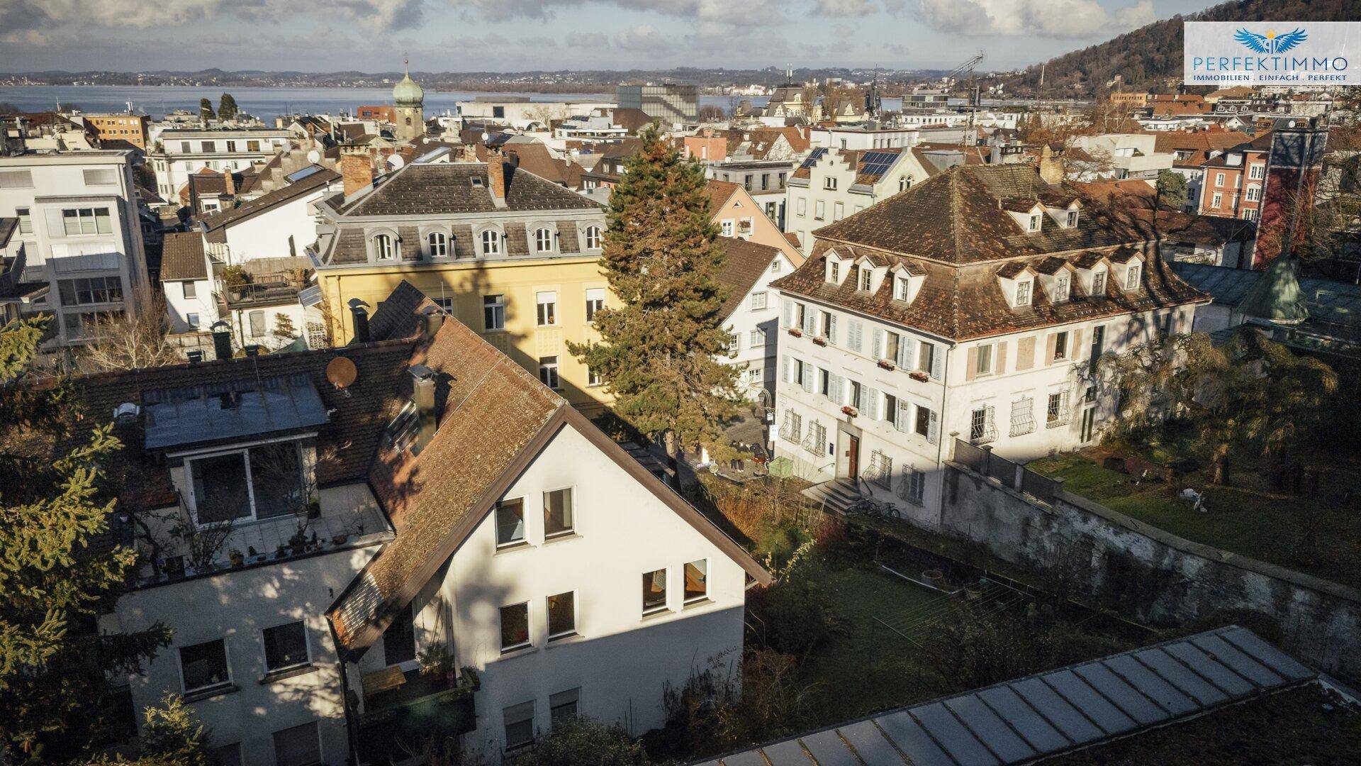 Panoramablick über eine Stadt mit vielen Häusern, einem See und Hügeln im Hintergrund.