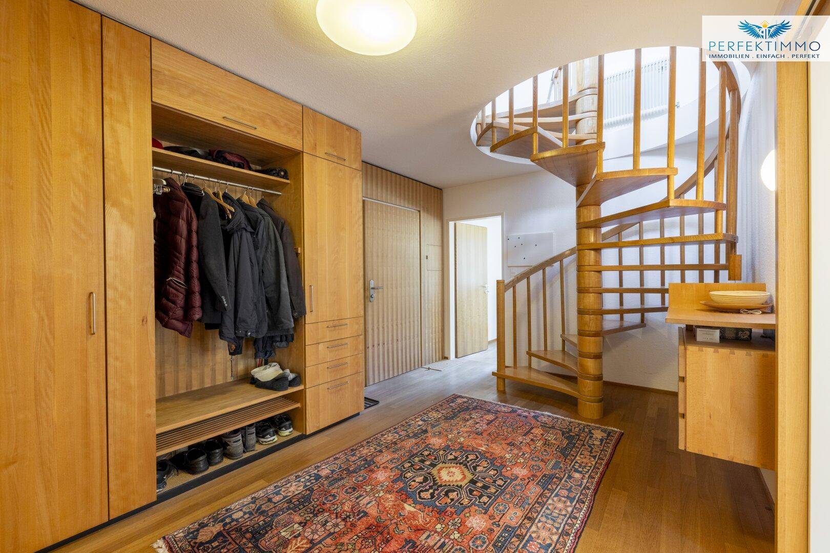 Heller Flur mit Einbauschränken aus Holz, einer eleganten Wendeltreppe und einem Teppich.
